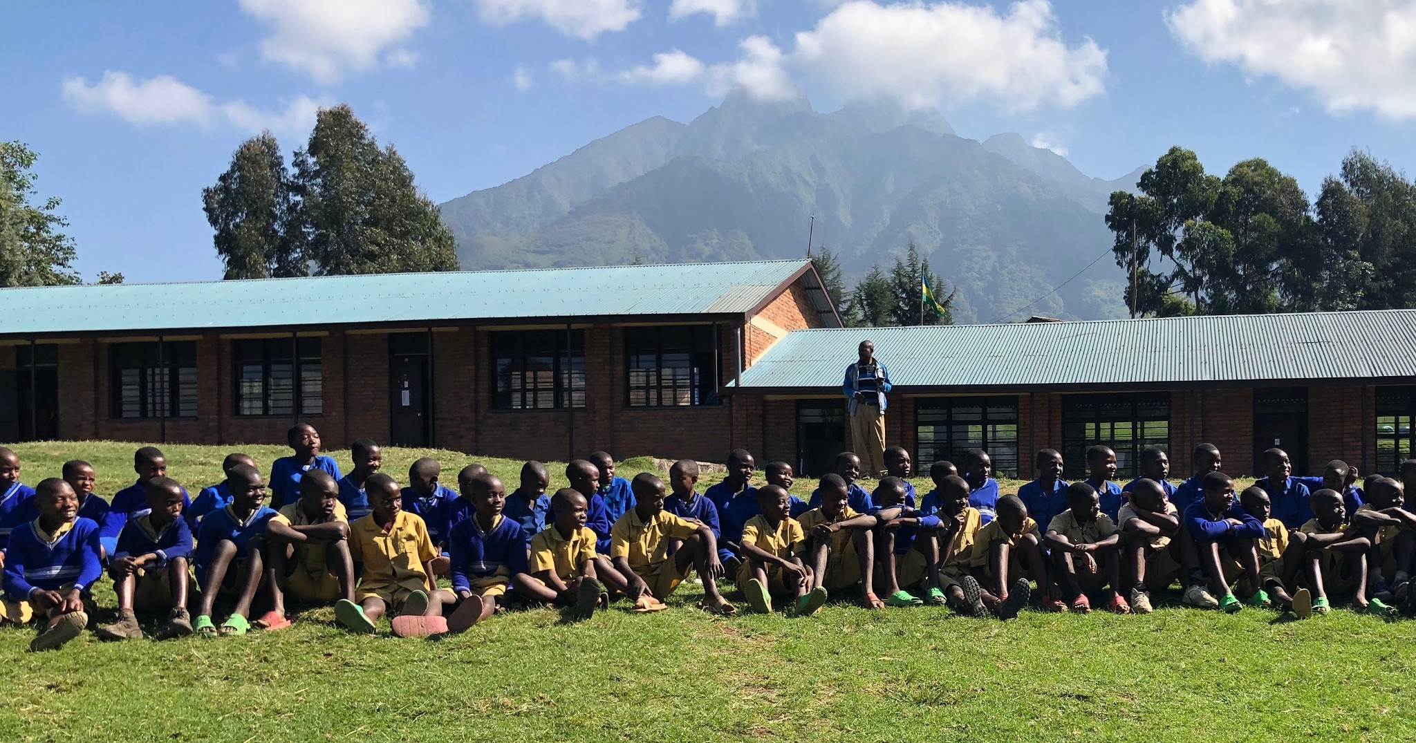 A large group of students sites in front of their school building.